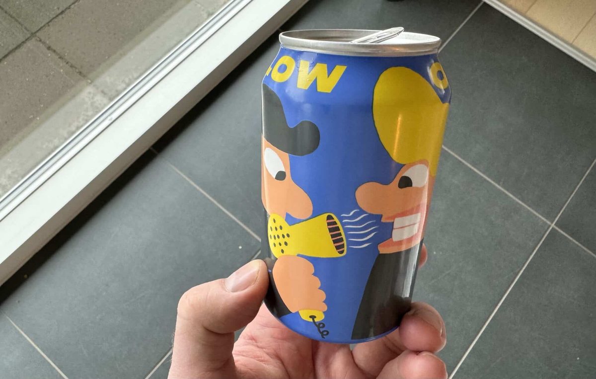 En åbnet blå dåse Blow Out fra Mikkeller holdes foran et mørkt klinkegulv