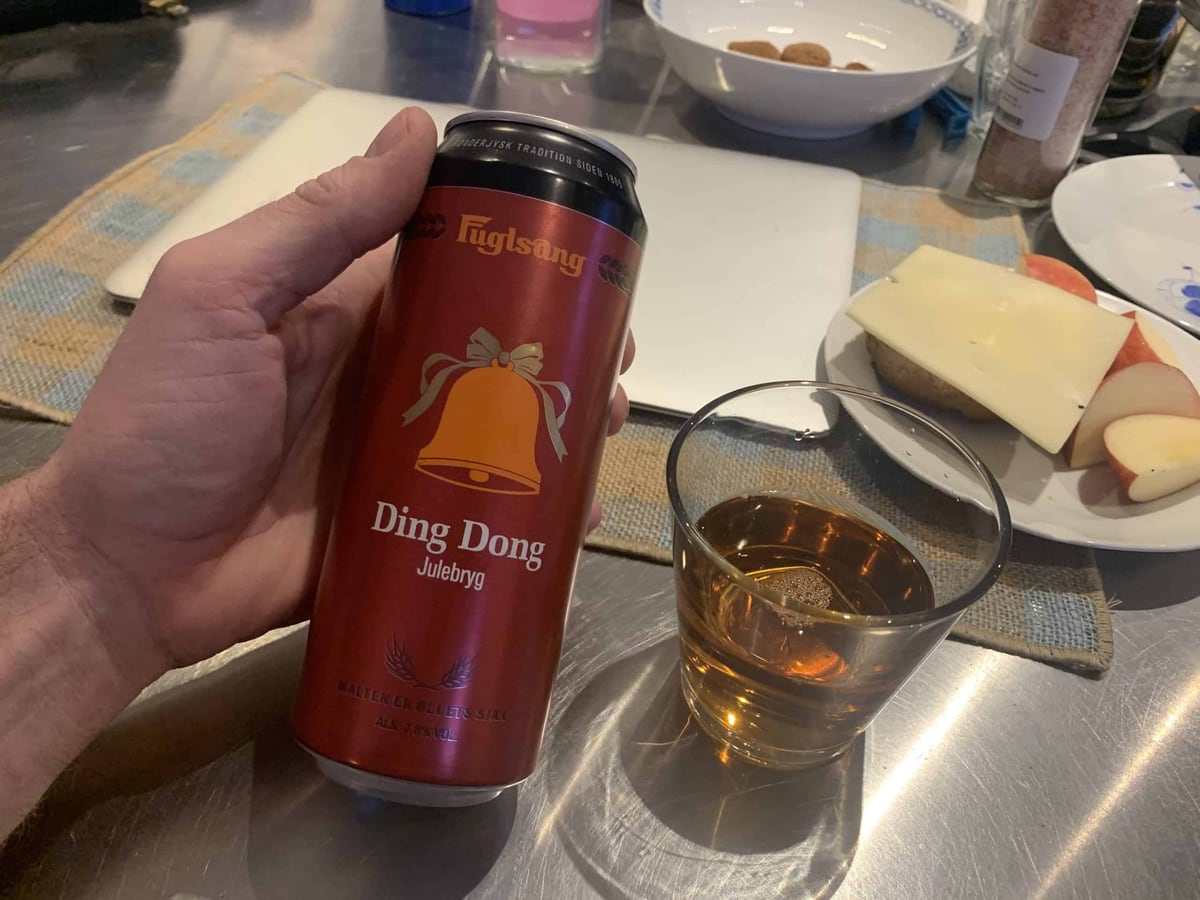 En rød dåse Fuglsang Ding Dong Julebryg holdes ved siden af et glas gylden øl og et fad med ost