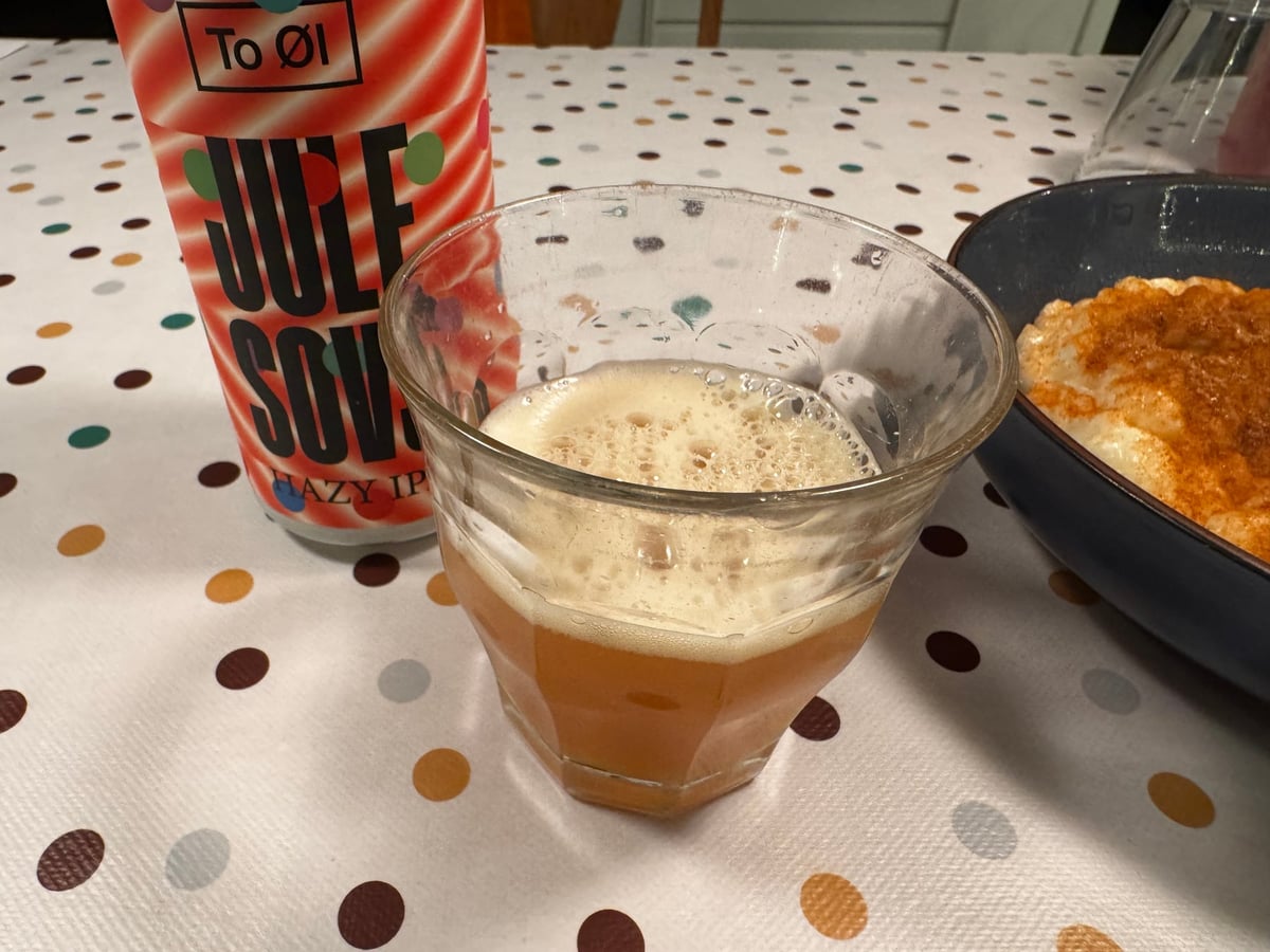Et glas uklar orangegylden Jule Sovs med dåsen og et måltid i baggrunden