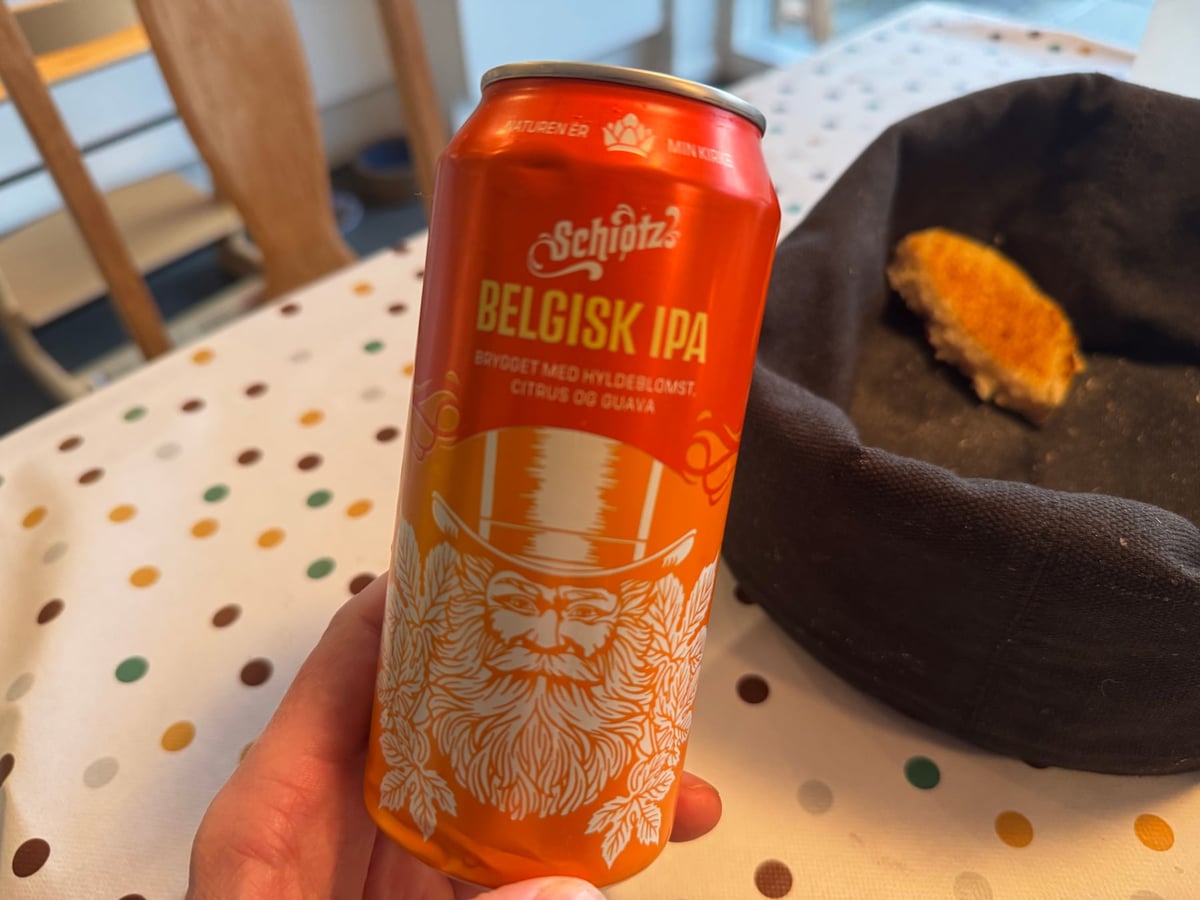 Orange dåse Schiøtz Belgisk IPA holdt over en prikket dug ved siden af en brødkurv