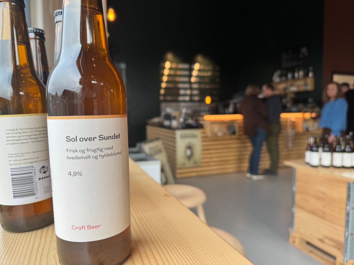 En flaske Sol Over Sundet står på en trædisk i Svendborgsund Bryghus med taproom i baggrunden